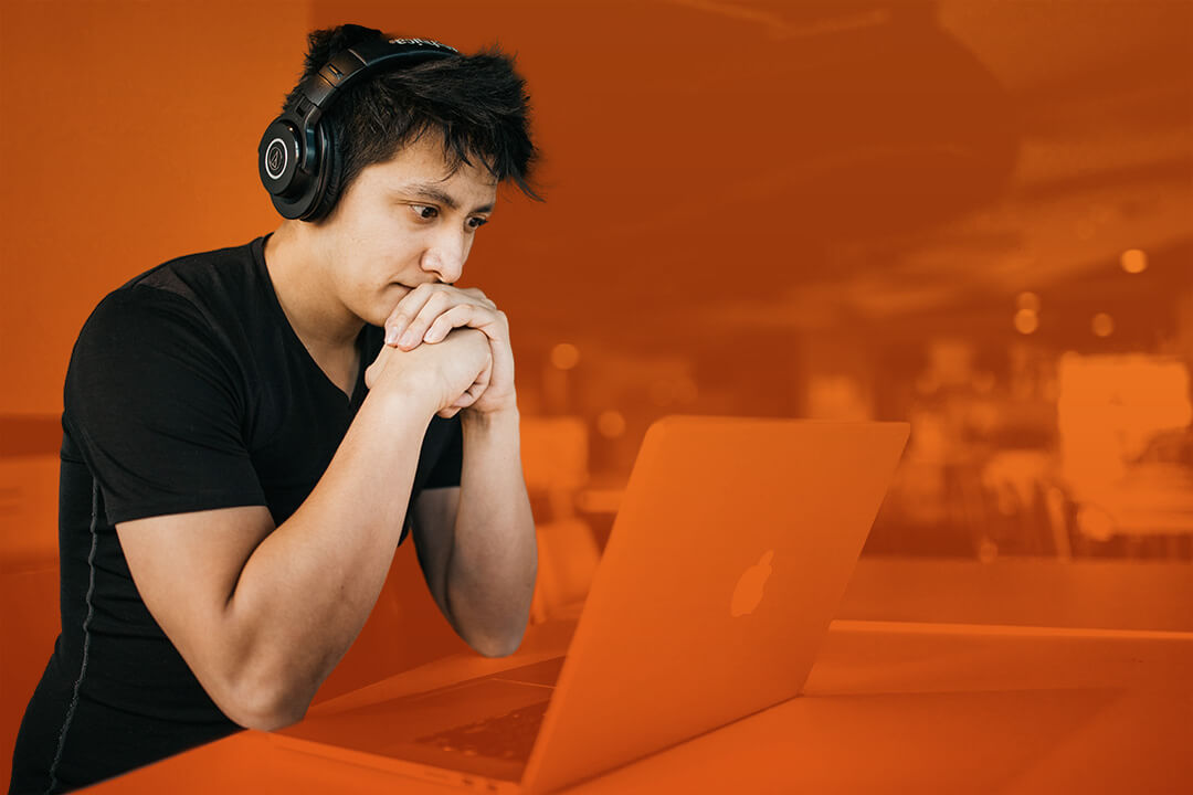 Junger Mann mit Kopfhörern der auf seinen Laptop schaut